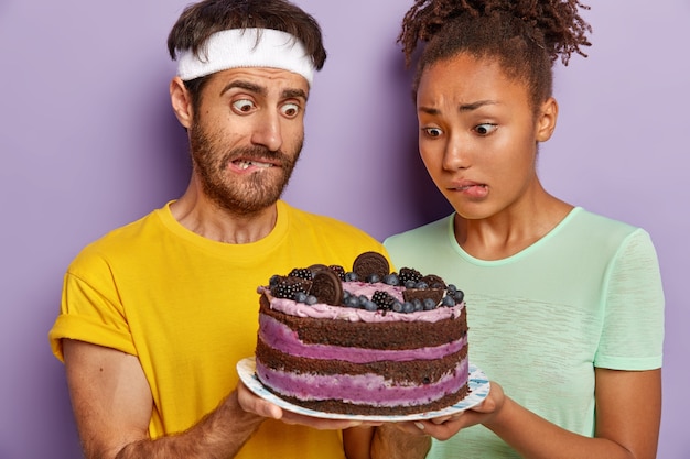 Puzzled active couple posing with a big cake