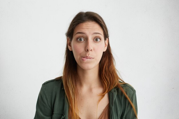 Puzzled beautiful woman with dark eyes and straight dyed hair biting her lower lip looking with surprise. Human face expressions and emotions.