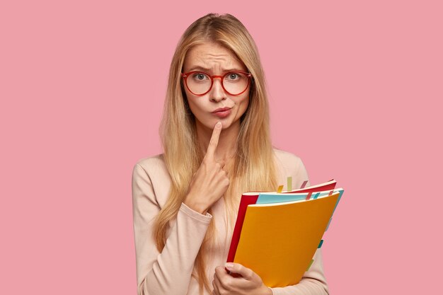 Puzzled blonde college student posing against the pink wall