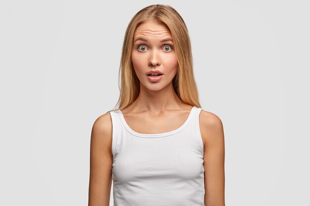 Puzzled blonde woman model looks with bewilderment, opens mouth slightly, has fear in eyes, dressed casually, has healthy skin