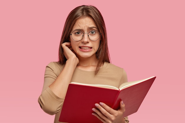 Free photo puzzled brunette teacher holds opened book in front