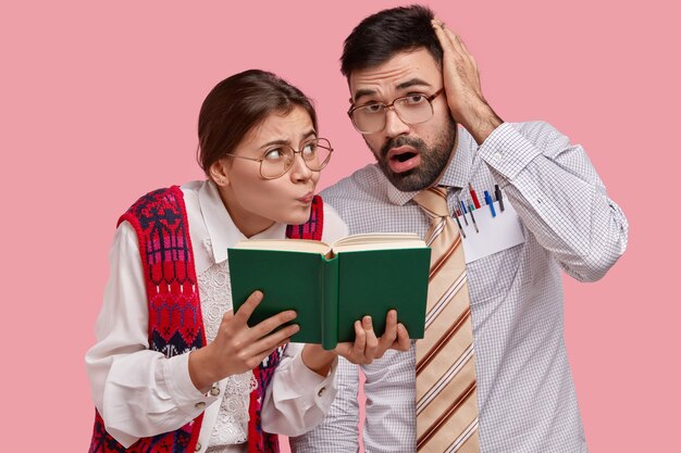 Puzzled clumsy female and male readers look at textbook, have worried expressions, cram material