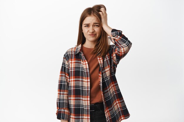 Puzzled girl student scratch head, squinting and grimacing perplexed, dont know, questioned about smth, have no idea, standing over white background