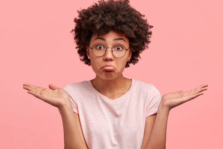 Free Photo puzzled hesitant african american female with clueless expression, curves lower lip, shrugs shoulders, dressed in casual outfit, poses against pink wall. dark skinned female can`t make decision