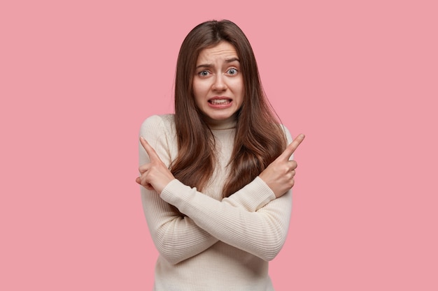 Free photo puzzled lady crosses hands over chest, points in different sides left and right, hesitates while makes important choice