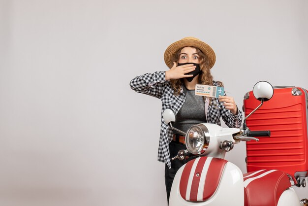 puzzled pretty woman holding ticket standing near moped red suitcase