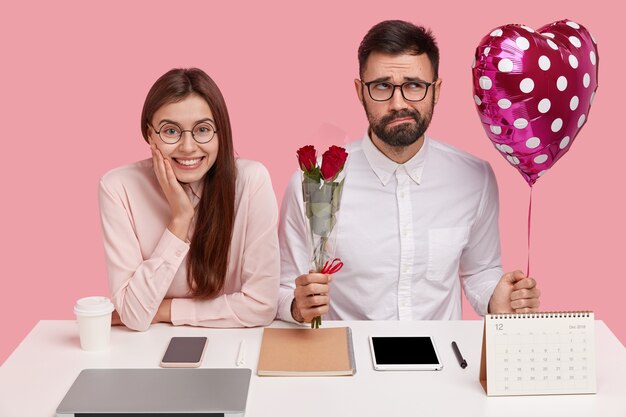 困惑したロマンチックな男は、女性の同僚に恋をして告白する前に適切な言葉を見つけようとし、赤いバラとバレンタインの花束を持っています