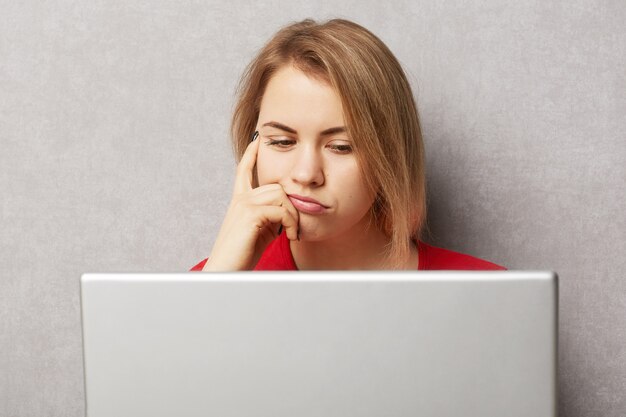 Озадаченная грустная молодая женщина читает информацию на веб-сайте через ноутбук