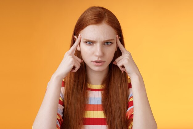 Puzzled serious-looking stressed-out young tired female student frowning look unhappy touching temples thinking trying focus, concentrate attention lecture memorizing hometask, orange background