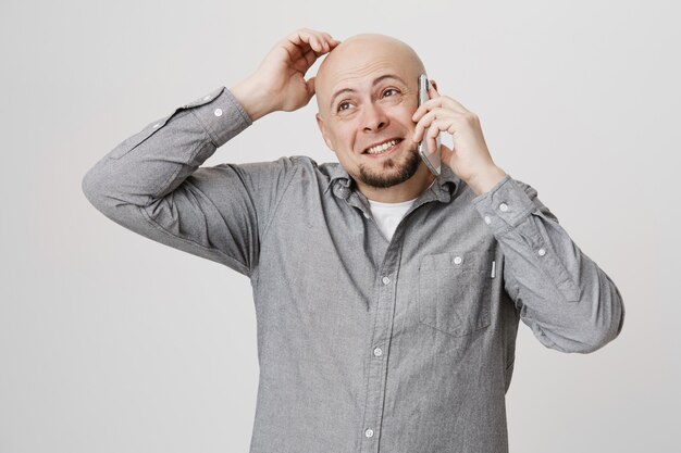 Puzzled thoughtful bald guy scratch head as talking on mobile phone