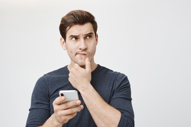 Free photo puzzled thoughtful man thinking while holding smartphone