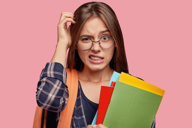 Free photo puzzled uncertain student posing against the pink wall with glasses