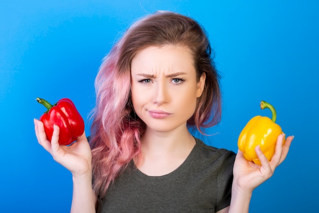 Foto gratuita donna perplessa che tiene i peperoni rossi e gialli in mani differenti