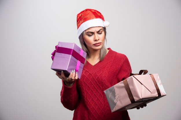 Puzzled woman in Santa hat looking at Christmas gifts.