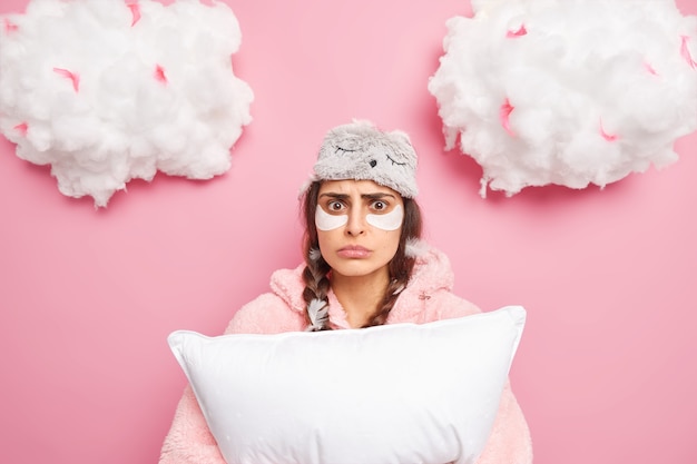 Puzzled worried woman has two pigtails awakes after seeing nightmare holds soft pillow