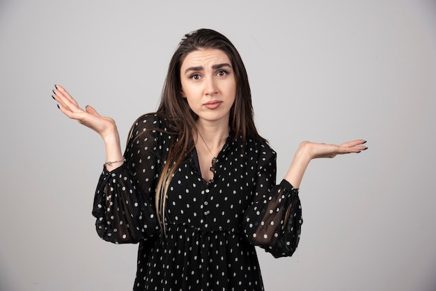 Puzzled young adult woman with arms out and shrugging her shoulders.