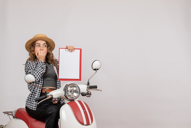 puzzled young girl on moped holding up clipboard on grey