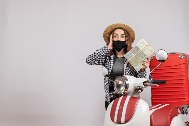 puzzled young girl with mask holding map standing near moped