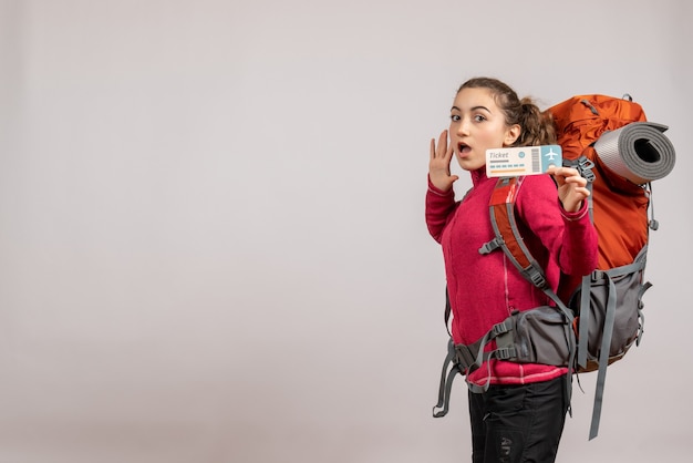 puzzled young traveller with big backpack holding up travel ticket