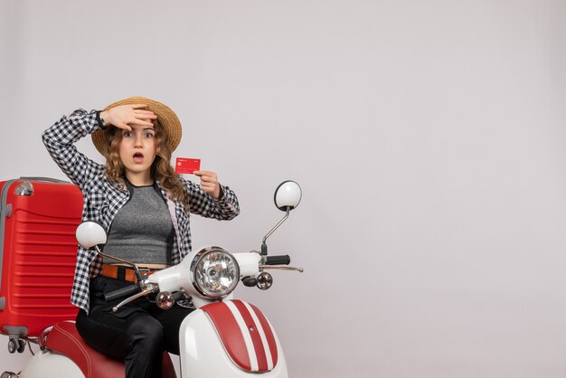 puzzled young woman on moped holding card on grey