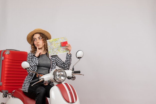 puzzled young woman on moped holding card and map on grey