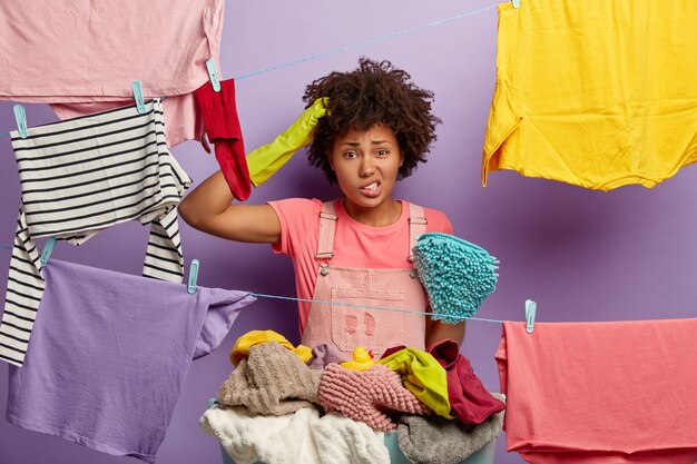 Puzzled young woman with an afro posing with laundry in overalls