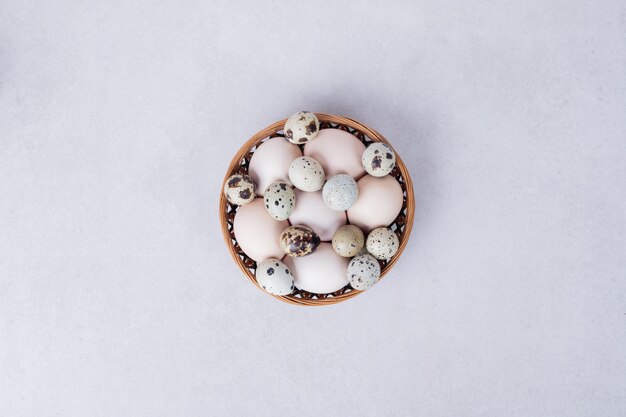 Quail eggs and chicken eggs in bowl on white surface.