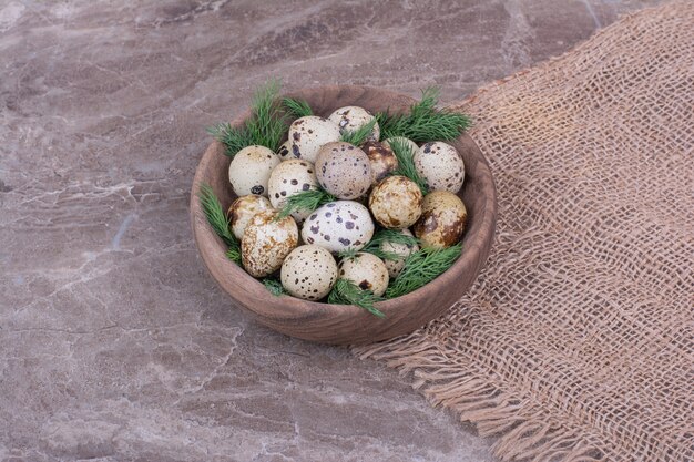 Quail eggs and herbs in a wooden cup.