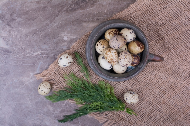 Quail eggs in a metallic pot on piece of burlap.