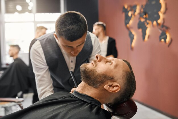 Qualified barber trimming beard of male client