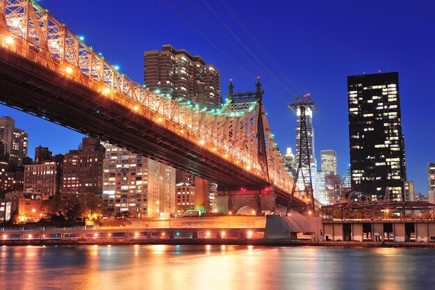 Queensboro Bridge over New York City East River at sunset with river reflections and midtown Manhattan skyline illuminated.