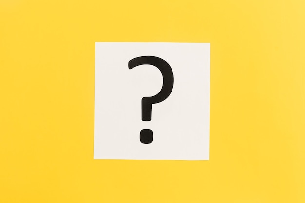 Free photo question mark on white paper on yellow background flat lay