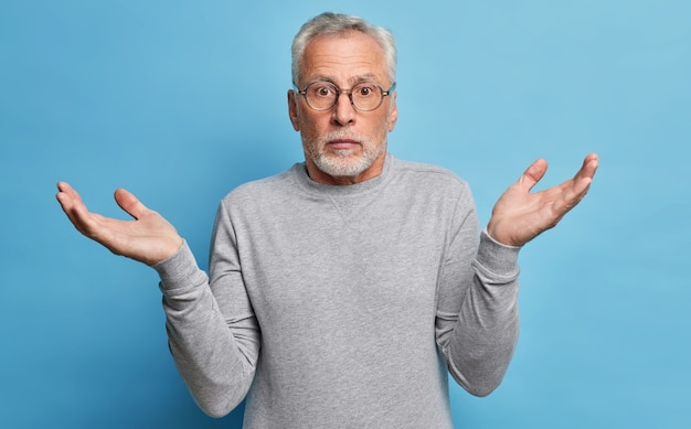Free photo questioned puzzled grey haired man spreads hands in clueless gesture shrugs shoulders has to make choice dressed in casual clothes cannot understand whats wrong looks with perplexed expression