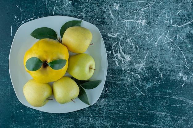 Айва и яблоки на тарелке, на мраморном фоне. Фото высокого качества