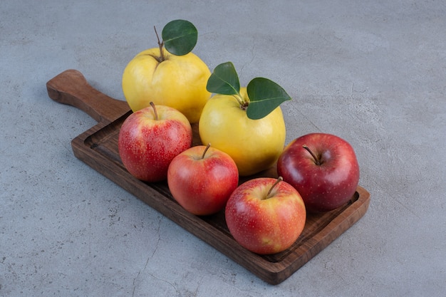 Quinces and apples bundled on a wooden board on marble background. 