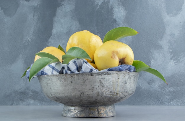 Quinces and leaves piled in a metal bowl on marble 