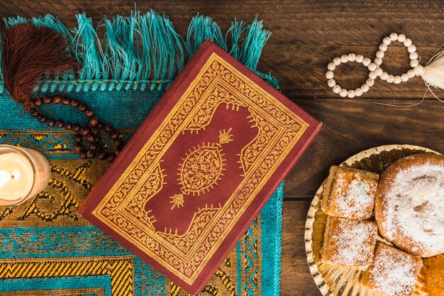 Quran and beads near candle and pastry