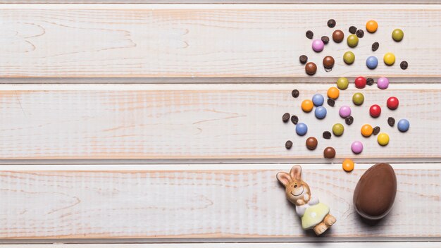 Rabbit figurine; easter egg; gem candies with chocolate chips on wooden desk