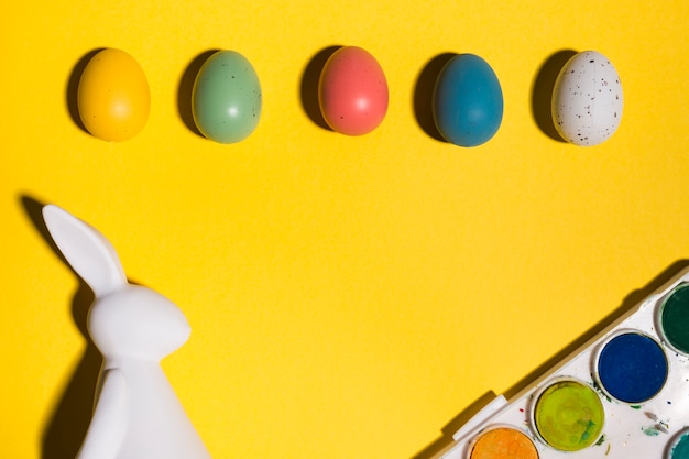 Free photo rabbit figurine with easter eggs and paints on table