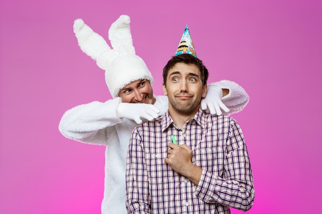 Free photo rabbit frightening drunk man over purple wall. birthday party.