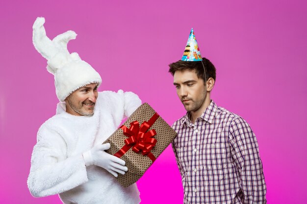 Кролик давая подарок на день рождения к пьяному человеку над фиолетовой стеной.