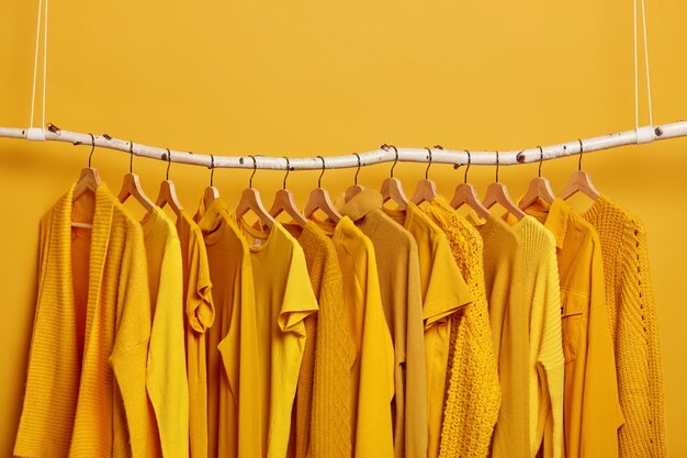 Rack with yellow clothes after dry cleaning. Wardrobe with various outfits for different seasons. Womens wear in fashion shop. Selective focus. Blank space above.