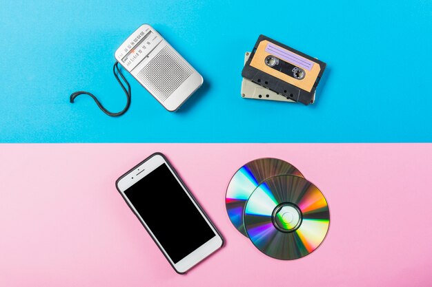 Radio; cassette; cd and cell phone on dual pink and blue colored backdrop