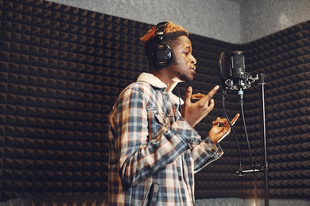 ラジオスタジオでポッドキャストを録音しながら身振りで示すラジオホスト。アフリカ人男性がレコーディングスタジオでリハーサルをします。