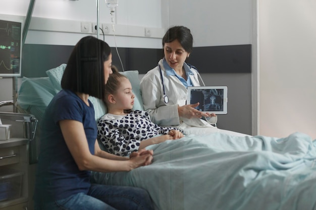 無料写真 病院の小児科病棟で休んでいる病気の少女のx線撮影スキャン画像を調べる放射線科の専門家。治療中の子供の脳の状態のx線スキャン結果を示す放射線科医。