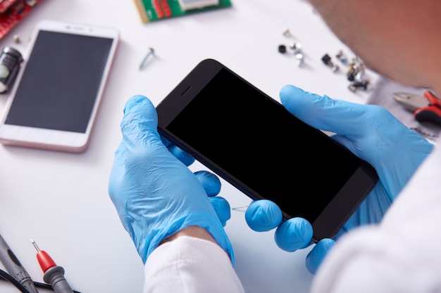 Free photo radiotrician with blue protective gloves holding smart phone with blank screen, trying to find cause of malfunction