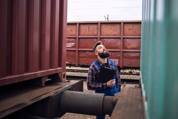 Foto gratuita ispettore ferroviario che controlla il treno merci alla stazione