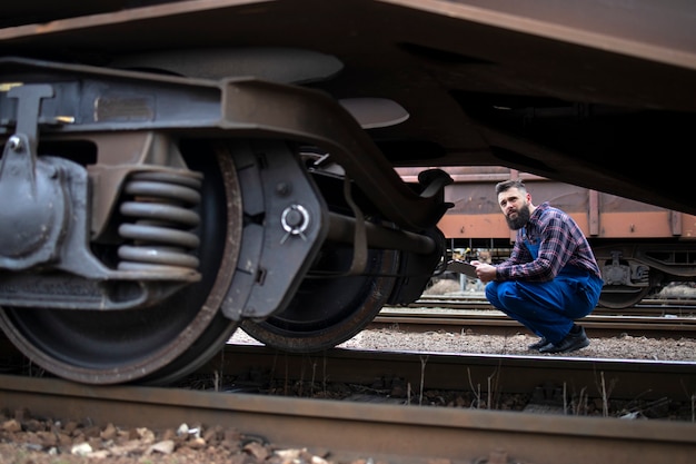 Foto gratuita operaio ferroviario che ispeziona ruote e freni del treno merci