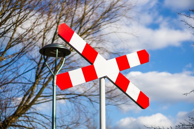 Railway crossing sign against bare trees and cloudy blue sky