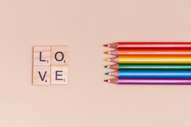 Радужные цветные карандаши и любовные буквы на бежевом фоне